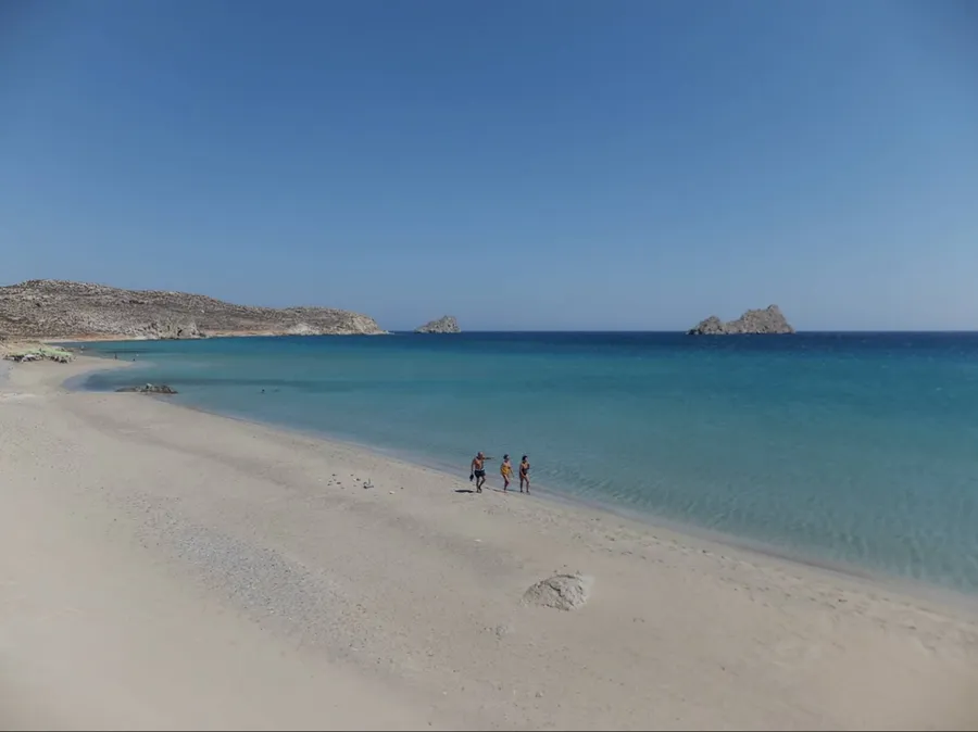 Large sandy beach with clear blue water and a few people walking at Xerokampos